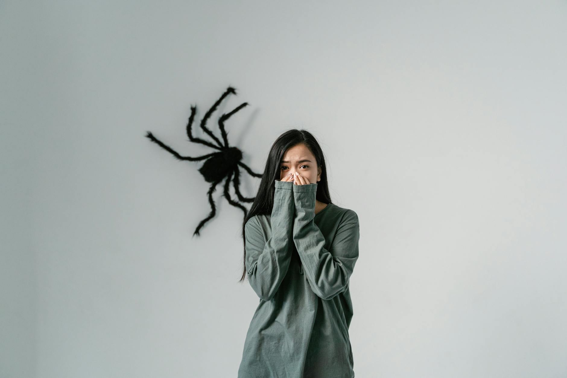 Woman covering her mouth, large black spider decoration on the wall behind her